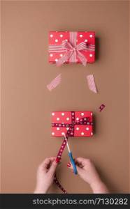 Woman hand cutting a ribbon and making gifts on brown background. Above view of gift wrapping concept. Christmas presents packaging. Birthday gifts.