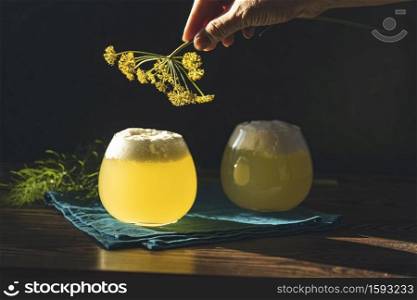Woman hand decorates fennel flower cocktail with fennel flower garnish. Scene is illuminated by beautiful evening sunlight.