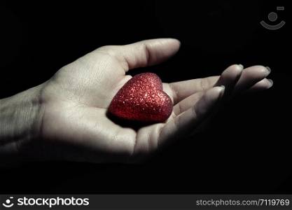 Woman hand holding a small heart as a symbol of love