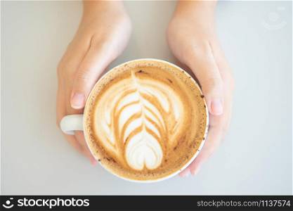 Woman hand holding a white coffee mug. Coffee is a latte. table on the wooden table in vintage style, taken from the top view, see the froth of milk foam.