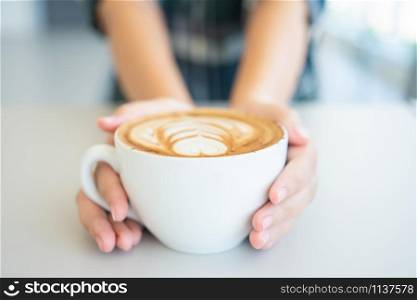 Woman hand holding a white coffee mug. Coffee is a latte. table on the wooden table in vintage style, taken from the top view, see the froth of milk foam.