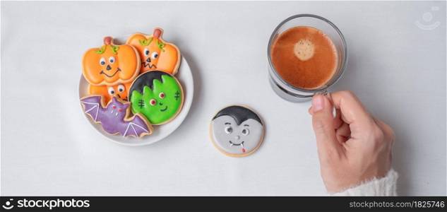 woman hand holding coffee cup during eating funny Halloween Cookies. Happy Halloween day, Trick or Threat, Hello October, fall autumn, Traditional, party and holiday concept