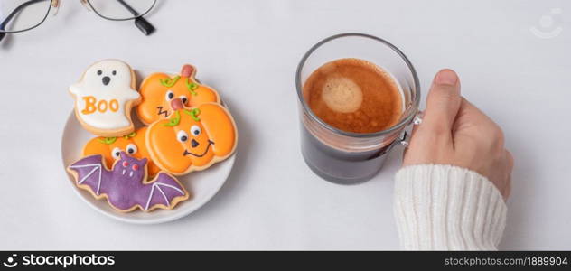 woman hand holding coffee cup during eating funny Halloween Cookies. Happy Halloween day, Trick or Threat, Hello October, fall autumn, Traditional, party and holiday concept