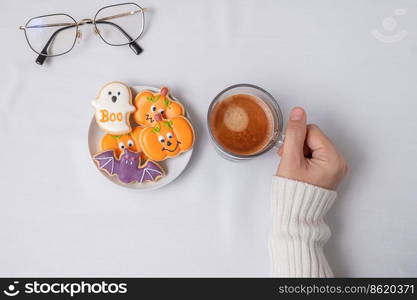 woman hand holding coffee cup during eating funny Halloween Cookies. Happy Halloween day, Trick or Threat, Hello October, fall autumn, Traditional, party and holiday concept