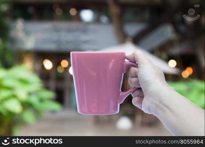 Woman hand holding coffee mug with cafe blurred abstract background