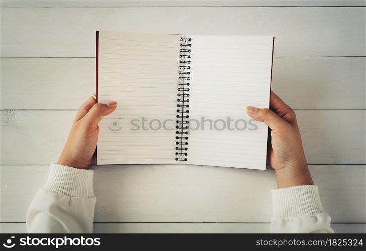 Woman hand holding empty open book on white wooden table. Empty paper page for add text