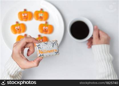 woman hand holding funny Halloween Cookie during drinking coffee. Happy Halloween day, Trick or Threat, Hello October, fall autumn, Traditional, party and holiday concept