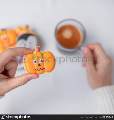 woman hand holding funny Halloween Cookie during drinking coffee. Happy Halloween day, Trick or Threat, Hello October, fall autumn, Traditional, party and holiday concept