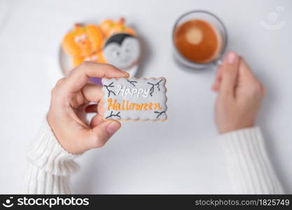 woman hand holding funny Halloween Cookie during drinking coffee. Happy Halloween day, Trick or Threat, Hello October, fall autumn, Traditional, party and holiday concept