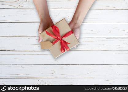 Woman hand holding gift box on wood plank and painted in white color with copy space.