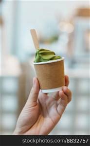 Woman hand holding green tea ice cream paper cup in cafe