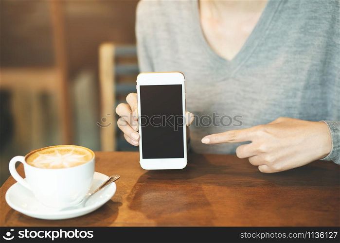 woman hand holding mobile smart phone with blank desktop screen and finger touching while drinking coffee in cafe shop.