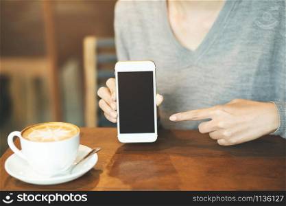 woman hand holding mobile smart phone with blank desktop screen and finger touching while drinking coffee in cafe shop.