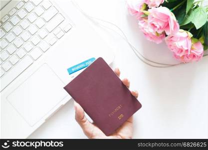 Woman hand holding passport and using laptop with pink rose, Overhead view on white background, Vacation concept