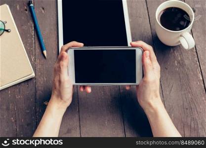 Woman hand holding phone and blank screen display on wood table in coffee shop.