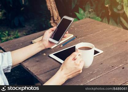 Woman hand holding phone and blank screen display on wood table in coffee shop.