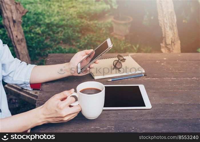 Woman hand holding phone and using phone on table in garden at coffee shop with vintage toned.