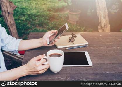 Woman hand holding phone and using phone on table in garden at coffee shop with vintage toned.