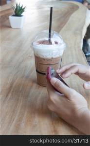 Woman hand holding phone with background of iced coffee, stock photo