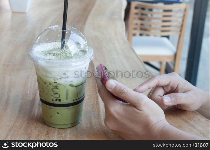 Woman hand holding phone with background of iced green tea, stock photo