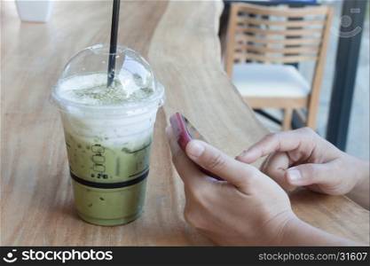 Woman hand holding phone with background of iced green tea, stock photo