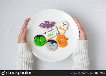woman hand holding plate of funny Halloween Cookies. Happy Halloween day, Trick or Threat, Hello October, fall autumn, Traditional, party and holiday concept