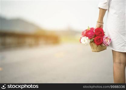 Woman hand holding rose flower hiding behind back side rear view to surprise couple on valentine’s day. Beauty woman giving surprise red rose florist outdoor in green park. valentine’s day concept
