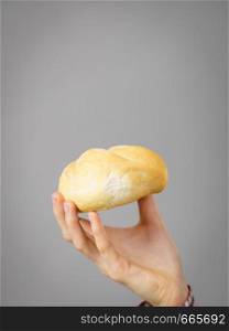 Woman hand holding small bun bread roll on gray background. Bakery products concept.. Woman hand holding bun bread roll.