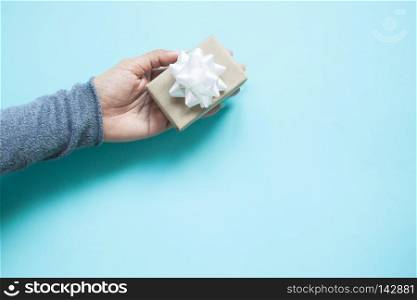 Woman hand holding small gift box on blue color background with copy space. Top view