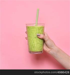 Woman hand holding smoothie shake against pink wall. Drinking green healthy smoothie concept.