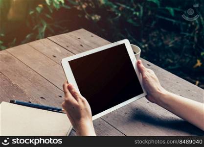 Woman hand holding tablet and blank screen display on wood table in coffee shop.