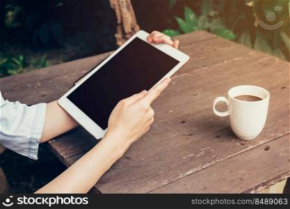 Woman hand holding tablet and blank screen display on wood table in coffee shop.