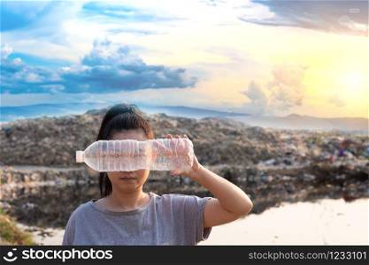Woman Hand holding use a clear plastic bottle to cover the face at mountain large garbage background, These waste come from urban and industrial areas can not get rid of, Pile of stink and toxic residue