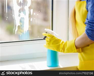 Woman hand in protective gloves washing cleaning windows during sunny weather. Using cleaner spray and cloth.. Woman hand cleaning window