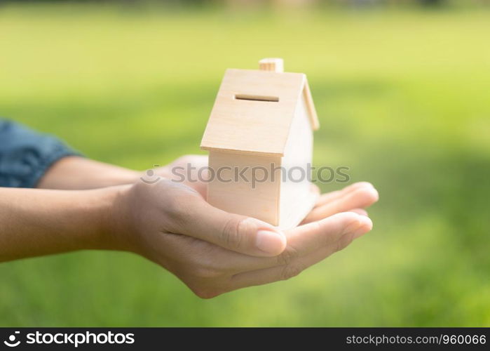 Woman hand is holding the wood house model on a blurred background in the public park