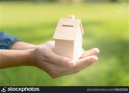 Woman hand is holding the wood house model on a blurred background in the public park