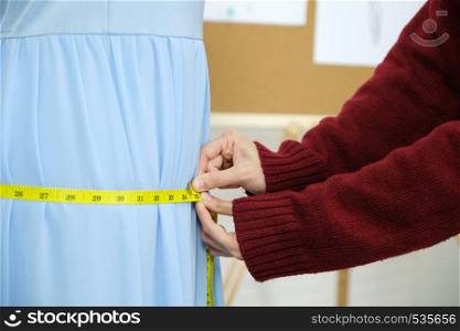Woman hand measuring blue dress, small business owner, fashion industry concept