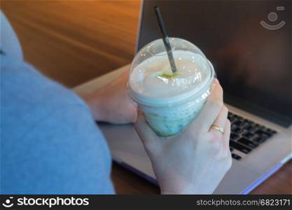 Woman Hand On Iced Milk Green Tea During Typing, stock photo