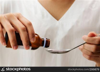Woman hand pouring medication or cough syrup from bottle to spoon. healthcare concept
