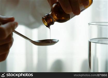 Woman hand pouring medication or cough syrup from bottle to spoon. healthcare concept