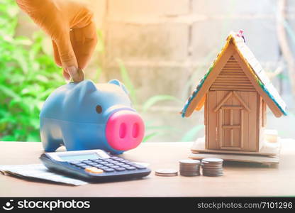 Woman hand put coin in piggy bank with coin stacks and house model, savings plans for housing