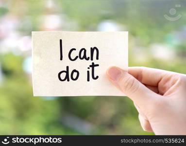 Woman hand showing I can do it texts on paper note on green nature background. Positive attitude, self belief and motivation concept.