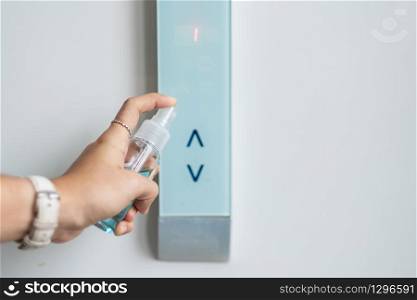 Woman hand spraying alcohol sanitizer bottle to the button control of elevator, against Novel coronavirus or Corona Virus Disease (Covid-19) at public indoor. Antiseptic,Hygiene and Healthcare concept