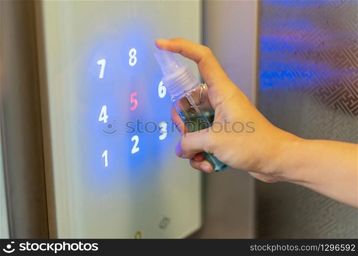 Woman hand spraying alcohol sanitizer bottle to the button control of elevator, against Novel coronavirus or Corona Virus Disease (Covid-19) at public indoor. Antiseptic,Hygiene and Healthcare concept