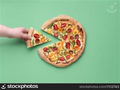 Woman hand taking a pizza slice. Delicious pizza primavera and eating context. Above view of spring pizza on green background. Italian tradition food