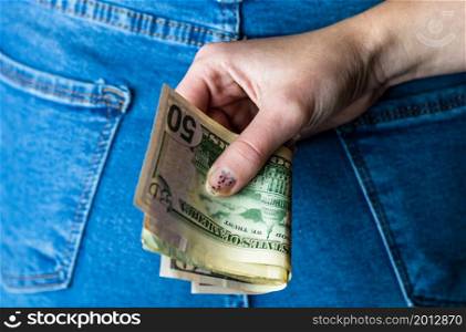 Woman hand taking money from jeans back pocket. Woman hiding money behind her back. Dollar banknotes close up