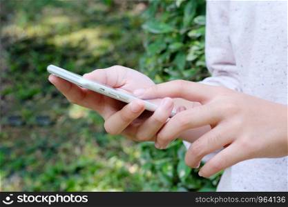 Woman hand using smart phone on green park background, business and technology concept, gen Z, digital marketing, lifestyle, the internet of things, social media network