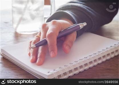 Woman hand with pen writing on notebook with vintage style