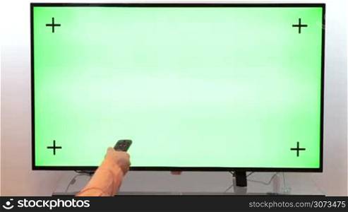 Woman hand with TV remote switching channels on a green screen TV point of view.