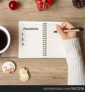 Woman hand writing checklist on notebook with black coffee cup and Christmas cookies on table. Xmas, Happy New Year, Goals, Resolution, To do list, Strategy and Plan concept
